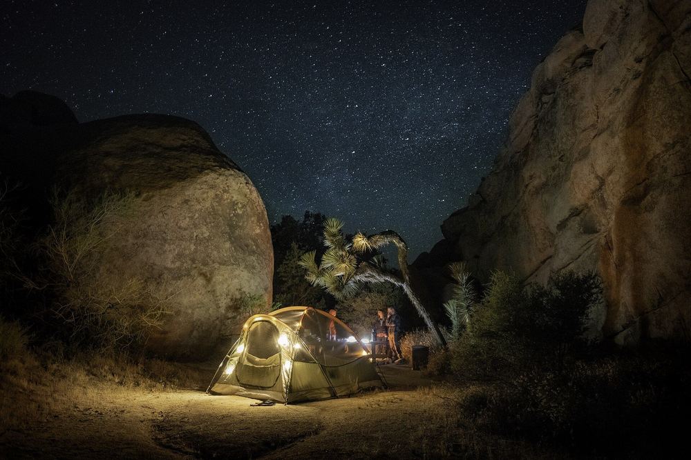 A lit tent among rocks under a night sky